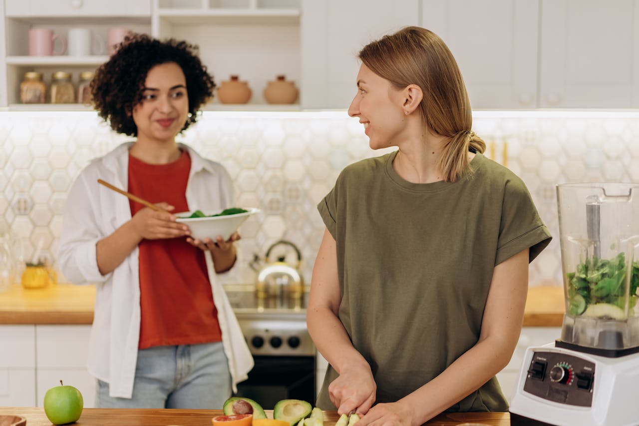 Two women happily preparing a fresh salad together in a home kitchen.